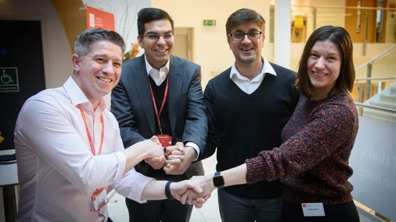 Three men and a woman smiling and shaking hands